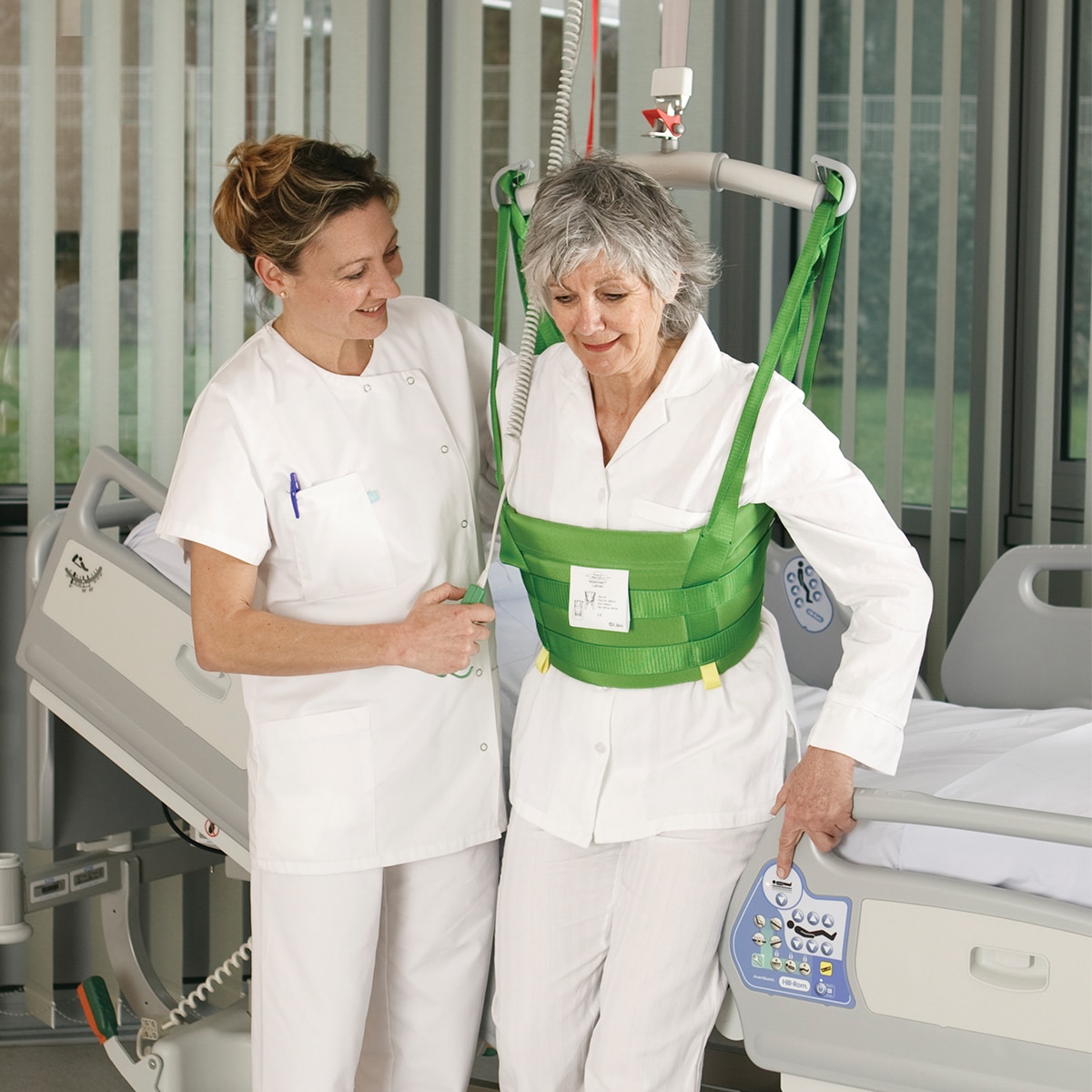 Hillrom 天井走行型リフトと MasterVest を使用して、病室で患者さんの歩行を補助する医師